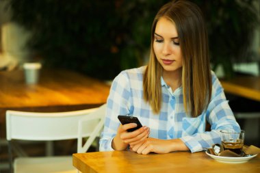 Genç güzel kadın kahve içme ve sabah haber tarafından sabah rahat bir kafede otururken cep telefonu internet bağlantısı okuma.