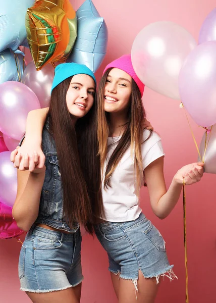 Zwei ziemlich emotionale Mädchen halten Luftballons und posieren gegen rosa Wand — Stockfoto