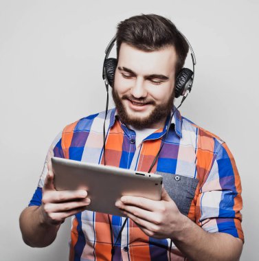 Açık gri arka planda kulaklık takan yakışıklı sakallı bir adamın stüdyo portresi..