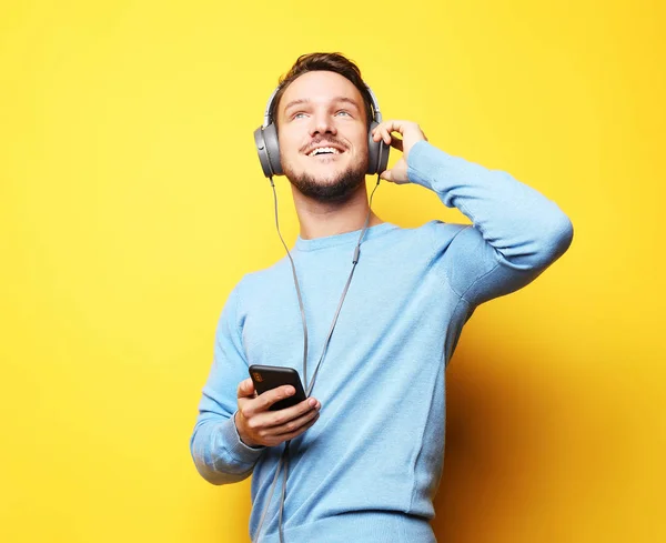 Joven usando auriculares y sosteniendo el teléfono móvil —  Fotos de Stock