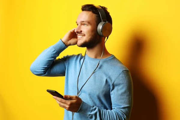 Mladý muž nosí sluchátka a drží mobilní telefon — Stock fotografie