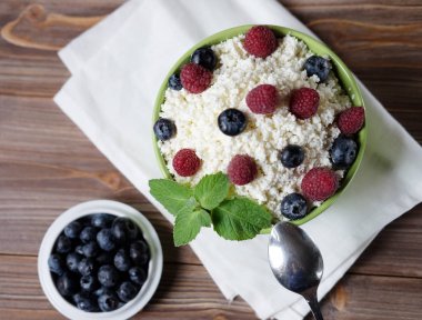Ahududu ve yaban mersini rustik ahşap arka plan üzerinde olgun çilek ile sağlıklı kahvaltı için bir kase süzme peynir. Üstten Görünüm.