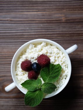 Ahududu ve yaban mersini rustik ahşap arka plan üzerinde olgun çilek ile sağlıklı kahvaltı için bir kase süzme peynir. T