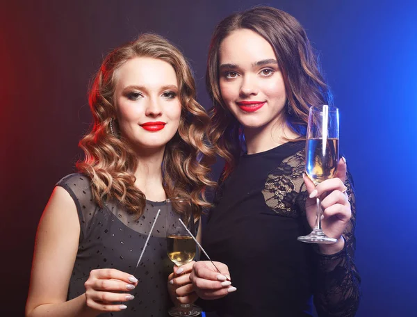 Partyzeit. zwei junge Frauen in schwarzem Kleid mit Weingläsern und funkelndem Feuer. — Stockfoto