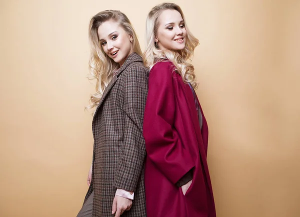 Fashion portrait of two girls, best friends posing indoor on beige background wearing winter stylish coat. — Stock Photo, Image