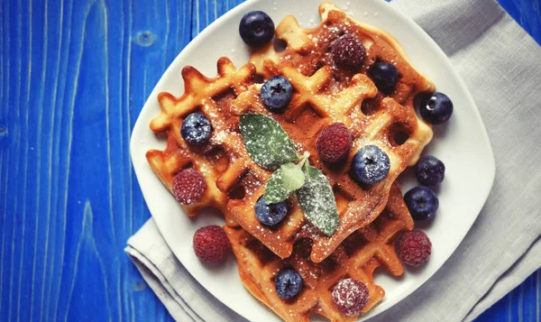 Geleneksel Belçika waffleları taze böğürtlenler ve beyaz tabakta şeker tozu, mavi ahşap arka plan. Düz konum, üst görünüm, kopyalama alanı. — Stok fotoğraf