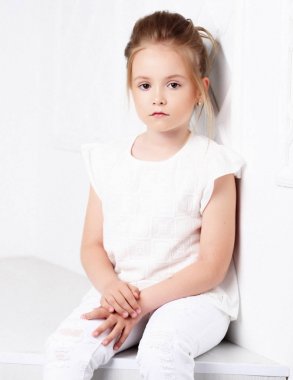 Çocuk moda. Oturma ve poz Beyaz giysili güzel dalgın ciddi sarışın kızı.