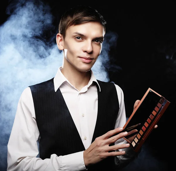 Professional makeup artist posing in studio, holds a palette of shadows. Against the background of smoke. — Stock Photo, Image