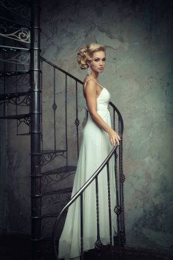 Beyaz elbiseli güzel genç gelin bir döner merdiven üzerinde duruyor. Düğün kavramı.