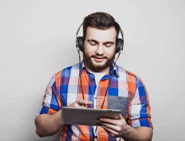 Açık gri arka planda kulaklık takan yakışıklı sakallı bir adamın stüdyo portresi..