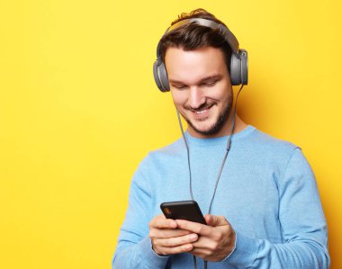 Kulaklık takan ve cep telefonu tutan genç bir adam.