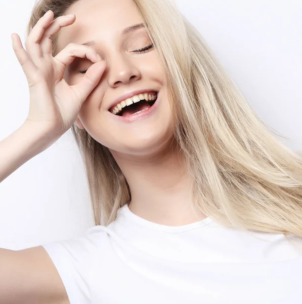 Estilo de vida y el concepto de la gente - Feliz mujer joven emocionada mirando a través del agujero hecho de sus dedos sobre el fondo blanco —  Fotos de Stock