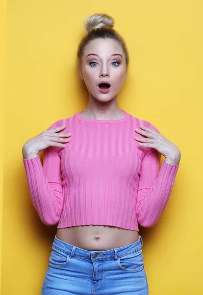 Surprised young blond woman shouting over yellow background. Looking at camera.