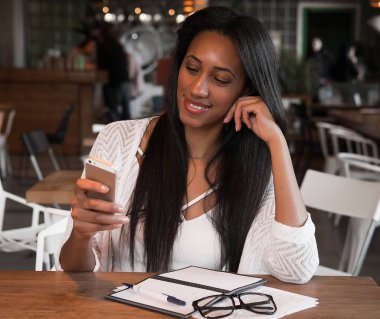 Yapılacaklar listesi yazmak ve getting haber Smartphone'da afro Amerikan hippi kız. Gülümseyen öğrenci ödev iyi haber üstünde hareket eden telefon ile bildirim okurken