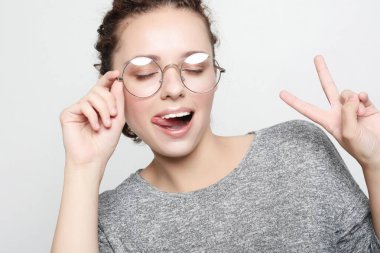 Gözlüklü kıvırcık kadın kameraya yüz ifadeleri takıyor, göz kırpıyor, dilini dışarı çıkarıyor..