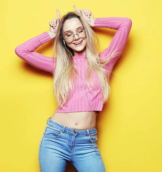 Portrait of a young beautiful girl on a yellow background with a smiling showing horns on the camera.