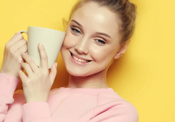 Wanita pirang muda memegang cangkir putih dengan teh atau kopi, gaya hidup dan konsep makanan. Tutup. Latar belakang kuning . — Stok Foto
