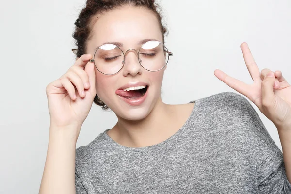 Curly woman wearing eyeglasses dressed casually making faces at camera, blinking, sticking out her tongue. — Stock Photo, Image