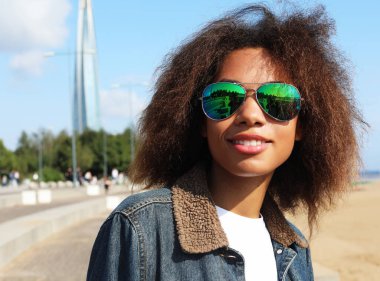 Güneş gözlüklü, açık havada poz veren, kısa, kaslı, kısa saçlı Afro-Amerikalı bir kız..