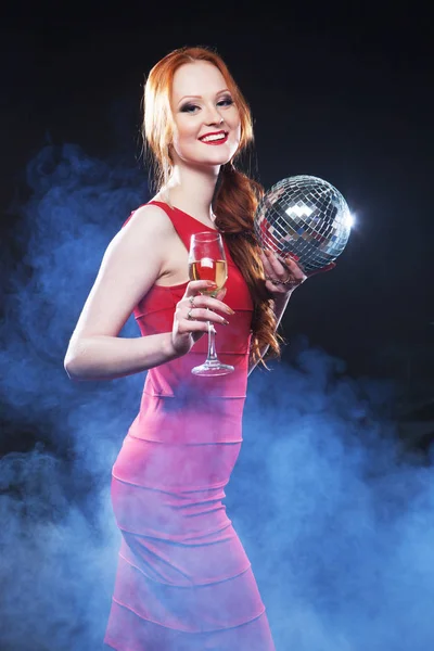 Junge sexy Frau in roten DRES hält Discokugel über dunklem Hintergrund — Stockfoto