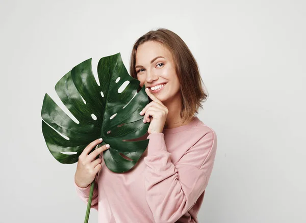 Hermosa joven sosteniendo una hoja de una gran flor tropical y sonriendo — Foto de Stock