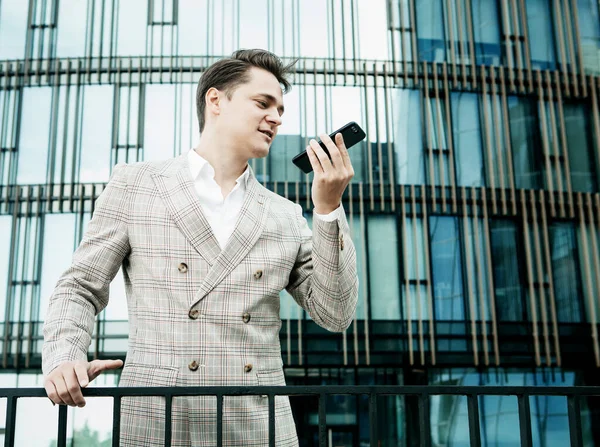 Young businessman dressed in formal clothes standing outside a glass building and using mobile phone — Stock Photo, Image