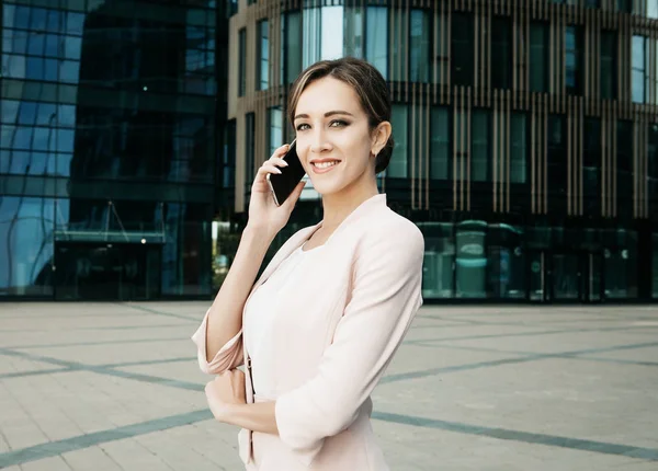 Hermosa joven mujer de negocios utiliza un teléfono móvil frente a un moderno centro de negocios — Foto de Stock