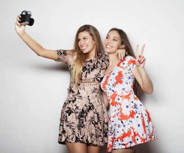 Yazlık elbiseler içindeki güzel genç kadınlar klasik bir kamera ile çekiliyor, beyaz arka plan.