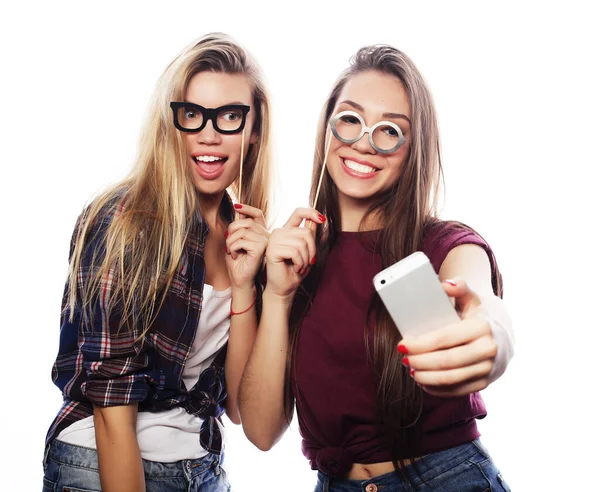 Zwei junge glückliche Frauen mit Partybrille machen Selfie mit Handy vor weißem Hintergrund — Stockfoto