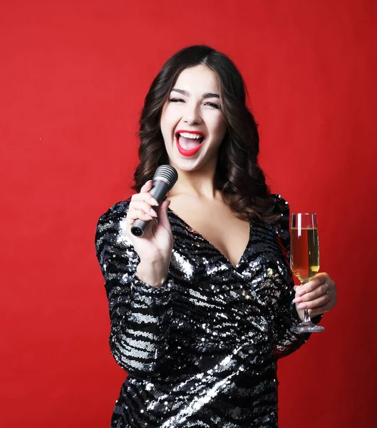 Giovane donna in abito da sera nero in possesso di un bicchiere di champagne e microfono. — Foto Stock