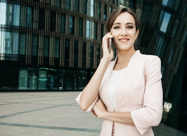 Hermosa joven mujer de negocios utiliza un teléfono móvil frente a un moderno centro de negocios — Foto de Stock