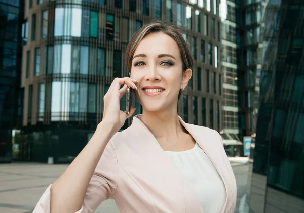 Hermosa joven mujer de negocios utiliza un teléfono móvil frente a un moderno centro de negocios — Foto de Stock