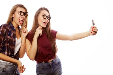 Parti gözlüklü iki genç mutlu kadın beyaz arka planda cep telefonlu selfie çekiyorlar.