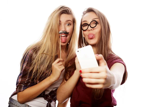 Дві молоді щасливі жінки з партійними окулярами беруть селфі з мобільним телефоном на білому тлі — стокове фото