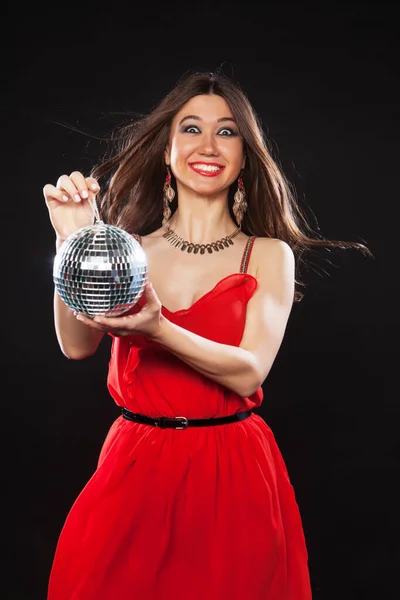 Jovem mulher sexy em vermelho dres mantendo bola de discoteca sobre fundo escuro — Fotografia de Stock