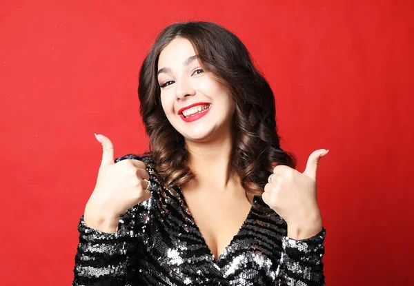 Retrato de una bonita mujer morena en vestido de noche mostrando signo de bien sobre fondo rojo — Foto de Stock