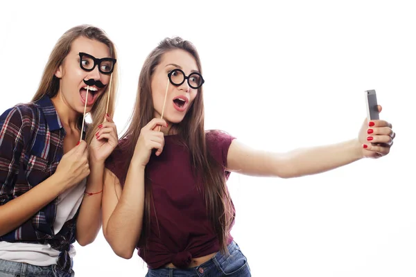 Zwei junge glückliche Frauen mit Partybrille machen Selfie mit Handy vor weißem Hintergrund — Stockfoto