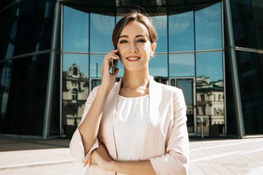 Genç iş kadını modern bir iş merkezinin önünde cep telefonu kullanıyor.