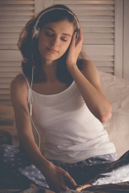 Genç kadın yatağında dinleniyor, müzik dinliyor.