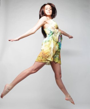 Gri sırt çantasının üzerinden atlayan şifon elbiseli çekici bir kadın.