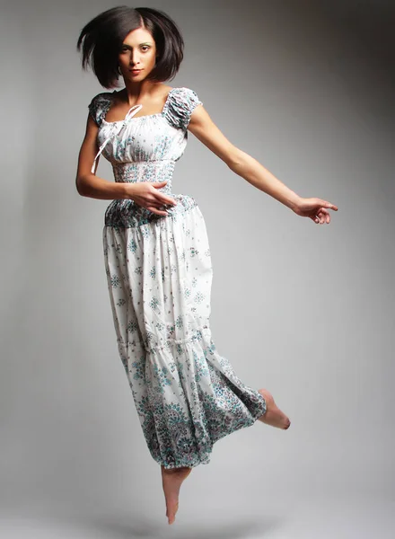 Молода чарівна жінка в шифоновому платті стрибає над сірим фоном — стокове фото