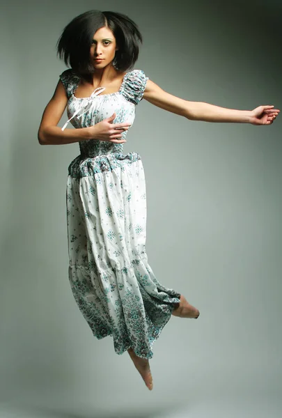 Молода чарівна жінка в шифоновому платті стрибає над сірим фоном — стокове фото