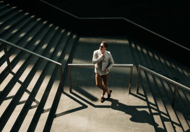 Gülümseyen genç iş adamı şehirde vakit geçiriyor, merdivenlerde dizüstü bilgisayar kullanıyor.