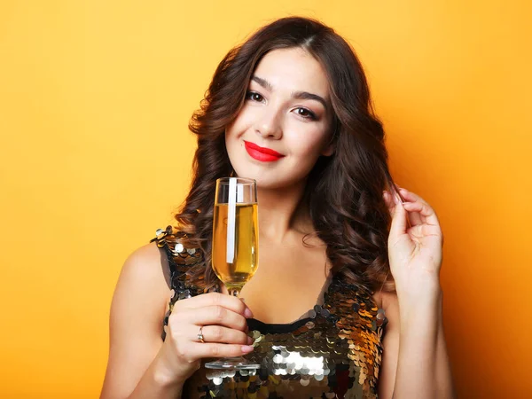 Žena ve večerních šatech drží sklo šampaňského přes žluté pozadí — Stock fotografie