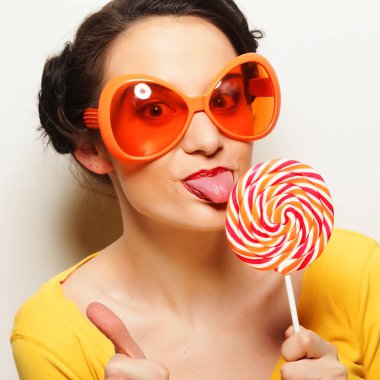 Büyük turuncu gözlüklü, elinde lolipop tutan komik bir kadın. Bir
