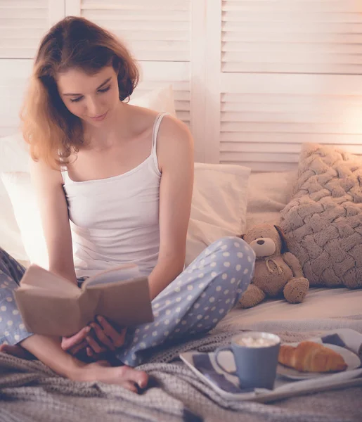 Дівчина в ліжку читає і п'є каву — стокове фото