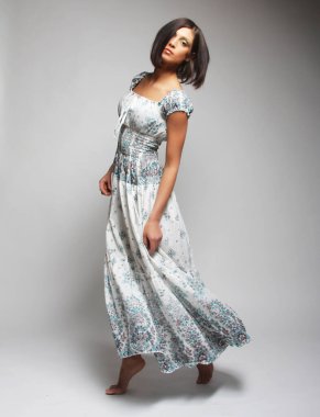 Gri sırt çantasının üzerinden atlayan şifon elbiseli çekici bir kadın.