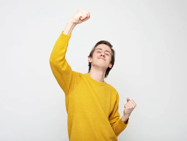 Ganar. Joven hombre guapo usar suéter amarillo con emociones en su cara sobre fondo blanco — Foto de Stock