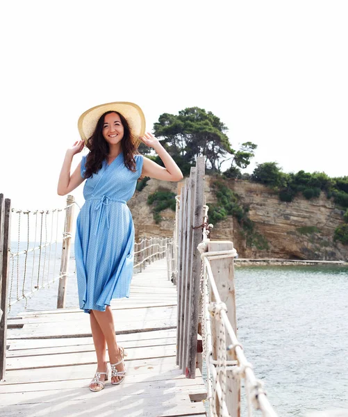 Mulher feliz vestindo vestido azul e chapéu na ponte perto do mar — Fotografia de Stock