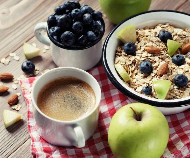 Sağlıklı bir kahvaltı yeni bir güne harika bir başlangıçtır. Tahta bir masada yulaf lapası, kahve, elma, böğürtlen ve fındık..